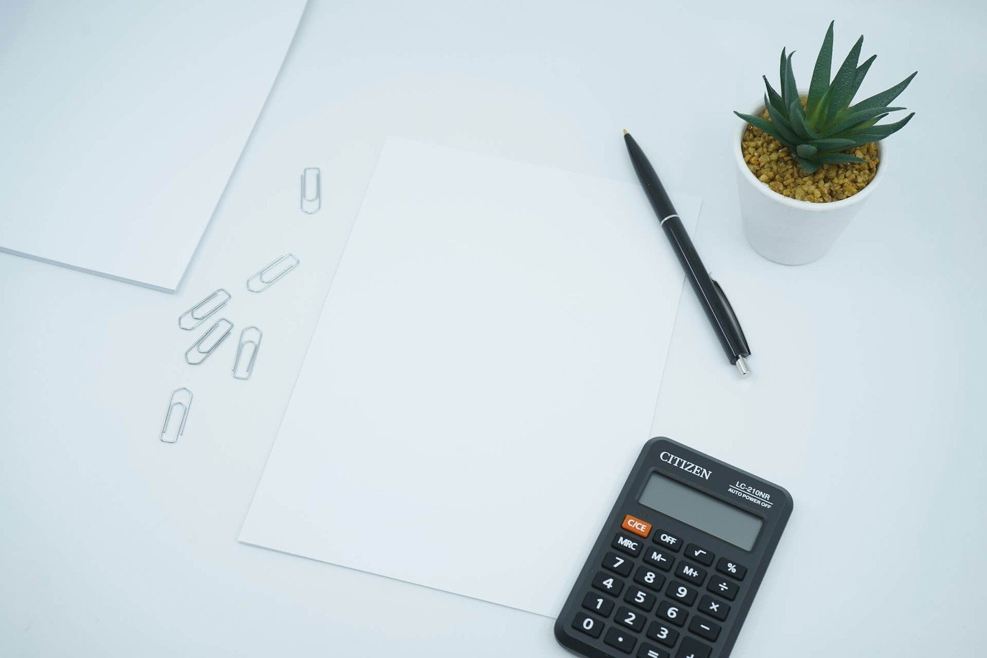 Calculator, pen and paper on a white desk